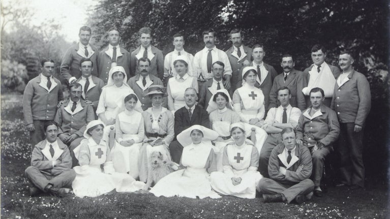 A black-and-white photograph showing a group of nurses and soldiers posed in a woodland.